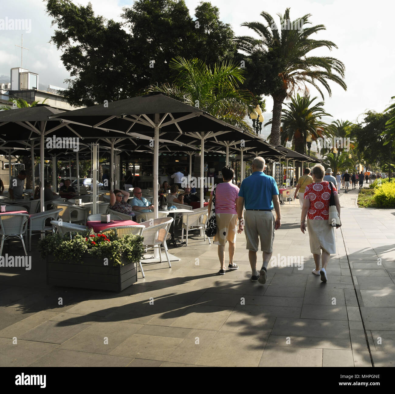 Drei Menschen zu Fuß hinter einem Cafe auf der Promenade in Funchal, der Hauptstadt von Madeira Stockfoto