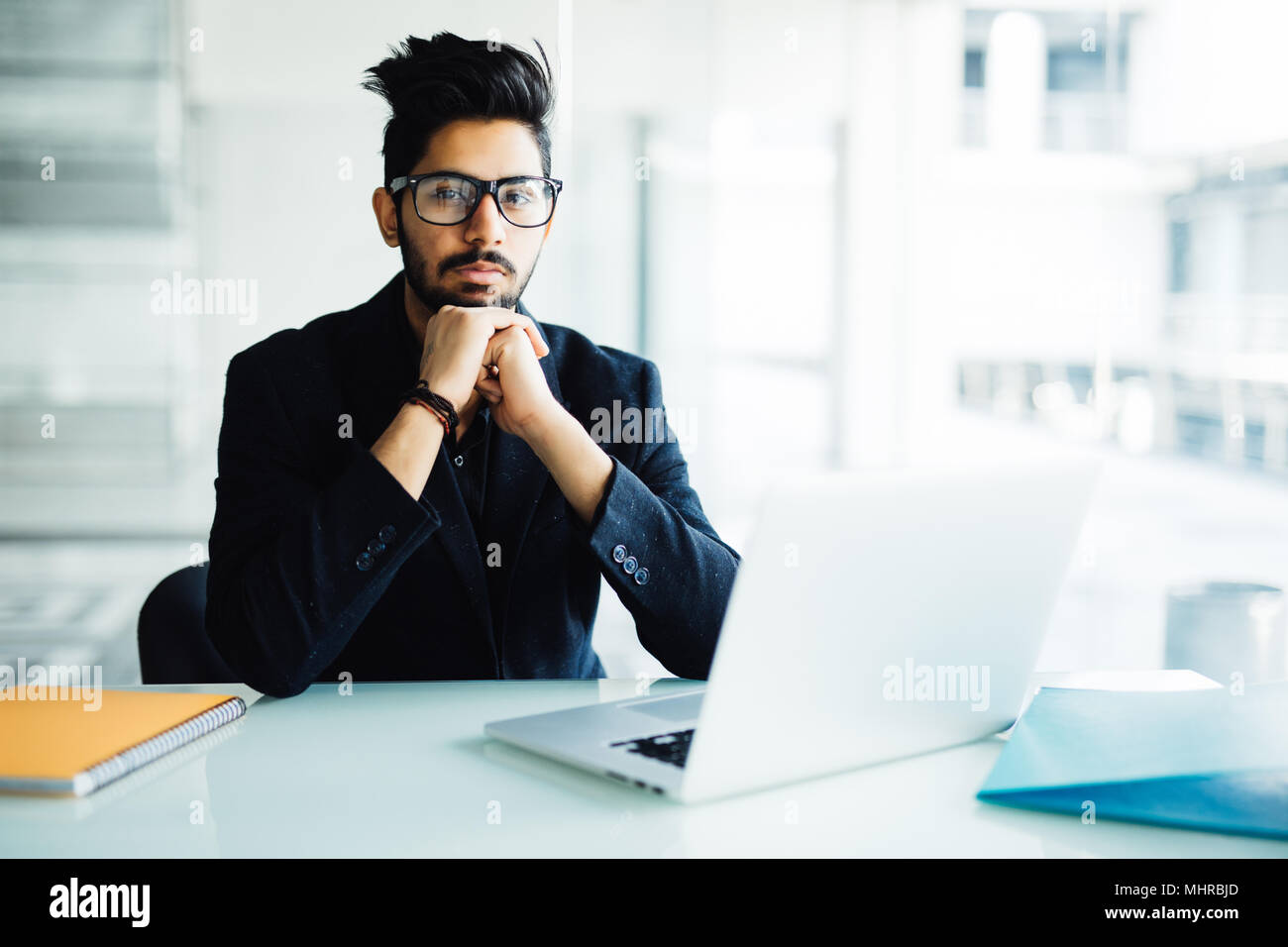 Indische Geschäftsmann mit Laptop mit Händen Hand am Kinn in seinem Büro Stockfoto