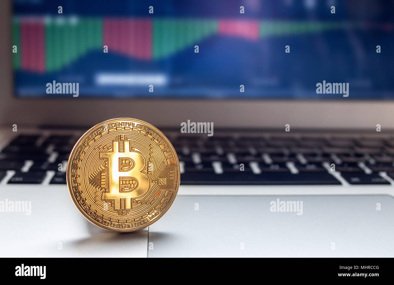 Physische Bitcoin auf Laptop mit Charts auf dem Bildschirm platziert Stockfoto