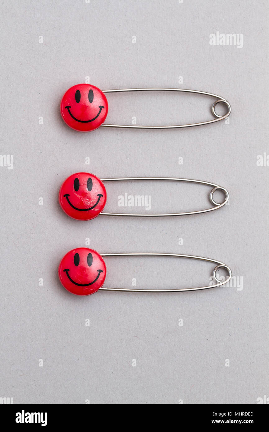 Kunststoff Kopf Metall safety Pins auf grauem Papier festgesteckt. Rot Lächeln emoticon Safety Pin. Nett und lustig bunte Emoticons. Stockfoto