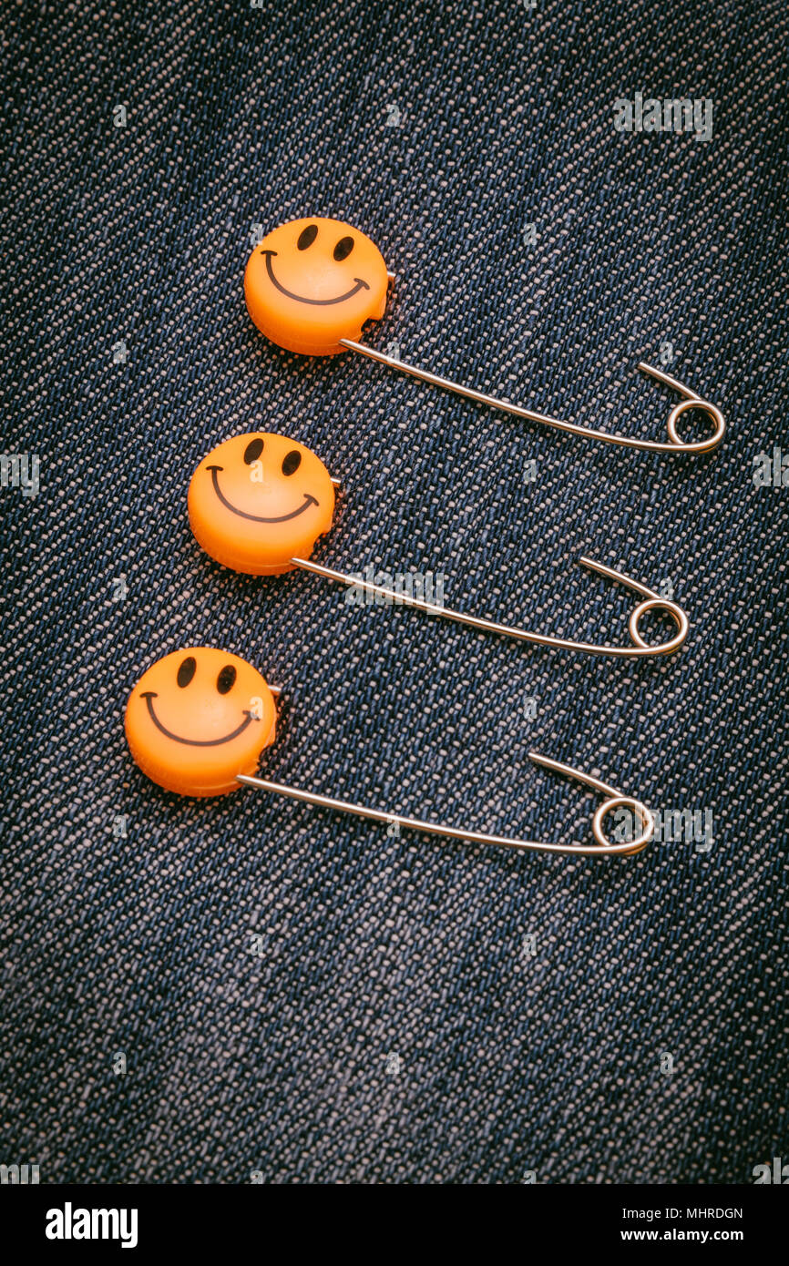 Kunststoff Kopf metall Sicherheitsnadeln in Jeans Material befestigt. Orange smile Emoticon Safety Pin. Nett und lustig bunte Emoticons. Stockfoto