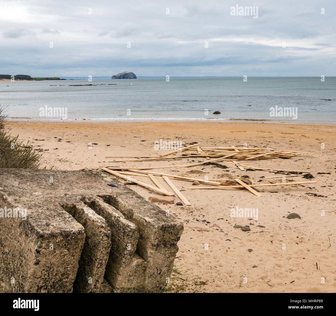 Ravensheugh Sands, East Lothian, Schottland, Vereinigtes Königreich, 2. Mai 2018. Ein sehr langweiligen, grauen Tag. Niemand am Strand mit einem abgenutzten konkrete Zweiten Weltkrieg Küstenschutz Straße Block, über den Firth von weiter in Richtung Bass Rock, Heimat der weltweit größten Northern gannet Kolonie. Planken von Holz liegen noch bis nach Verschütten von Cargo Schiff "Friesischen Lady', die das Holz Bundles bei strengem Wetter am 2. März während der 'Tier verloren aus dem Osten' gewaschen Stockfoto