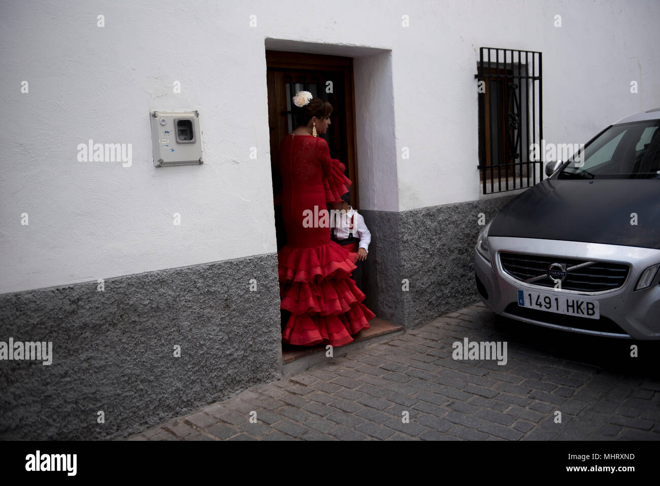 Eine Frau, die ihren Sohn tragen mit typischen Flamenco Kleid in einer Straße von Albaicin Viertel gesehen, während die Dia de Las Cruces in Granada." El Día de la Cruz" oder "Día de las Cruces" ist eines der schönsten Feste in Granada. Jeder dritte Mai viele Straßen, Plätze und Terrassen zeigen Altäre mit Kreuzen geschmückt mit Blumen zum Heiligen Kreuz zu gedenken. Stockfoto