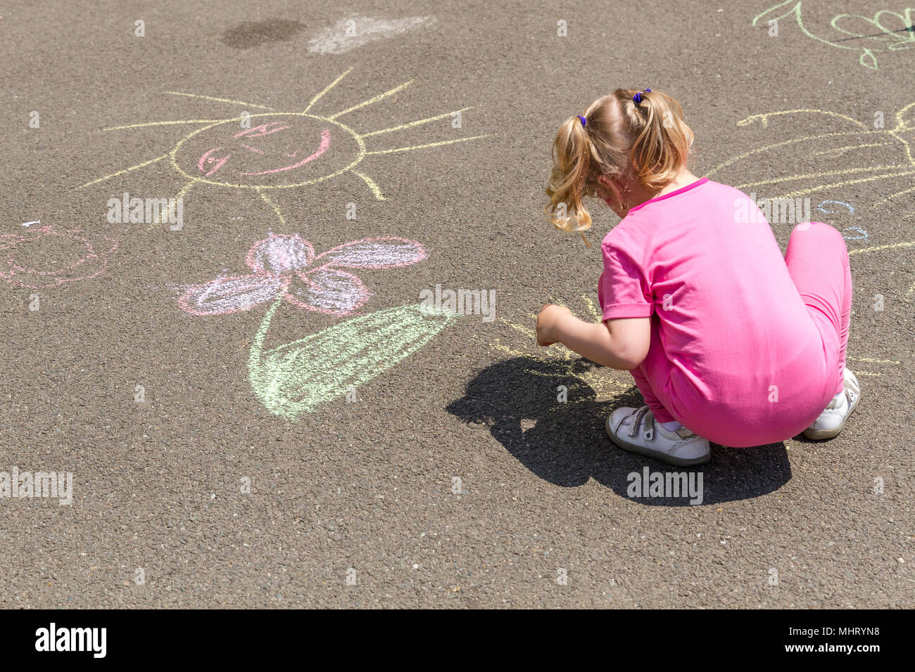Junge blonde Mädchen in rosa Tuch Zeichnen mit Kreide auf Asphalt. Bild in einem Park, an einem sonnigen Tag des Sommers. Stockfoto