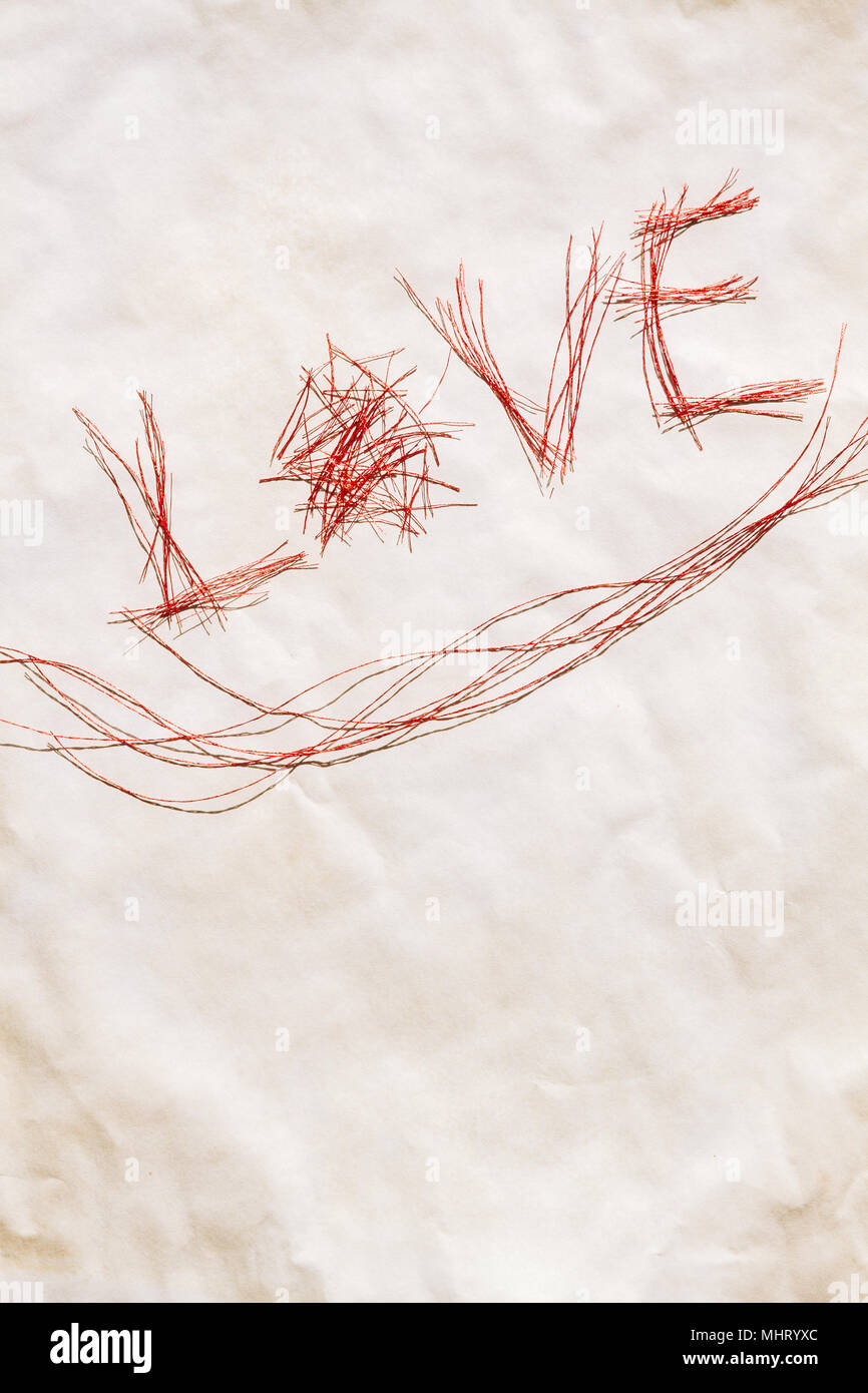 Wort Liebe aus vielen kleinen glänzenden roten Fäden auf weißem Papier zerknittert grungy. Stockfoto