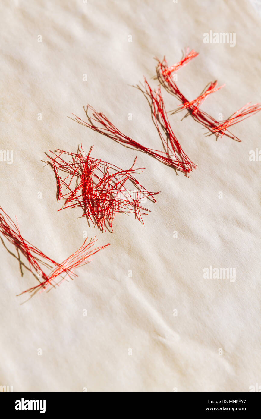 Wort Liebe aus vielen kleinen glänzenden roten Fäden auf weißem Papier zerknittert grungy. Stockfoto