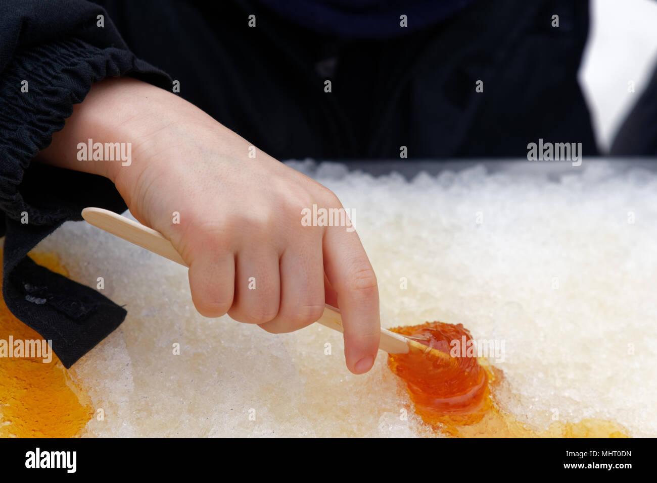 Nahaufnahme von der Hand eines Jungen (5 Jahre alt) Kind rolling Ahornsirup taffy auf einen Stick Stockfoto