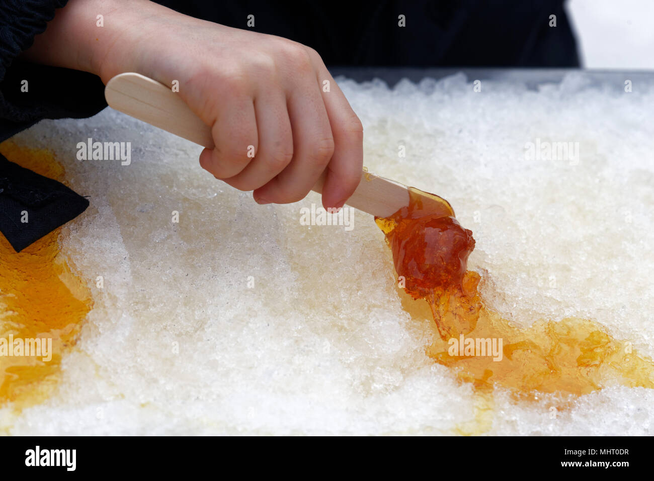 Nahaufnahme von der Hand eines Jungen (5 Jahre alt) Kind rolling Ahornsirup taffy auf einen Stick Stockfoto