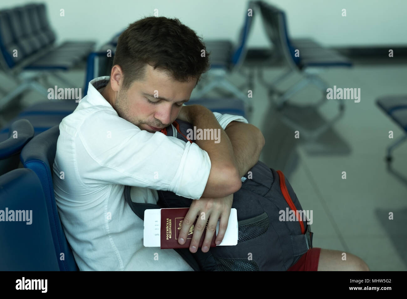 Kaukasische Mann in Flughafen Nickerchen. Er hält seinen Pass und Tickets. Russische Föderation ist auf Dokument geschrieben Stockfoto