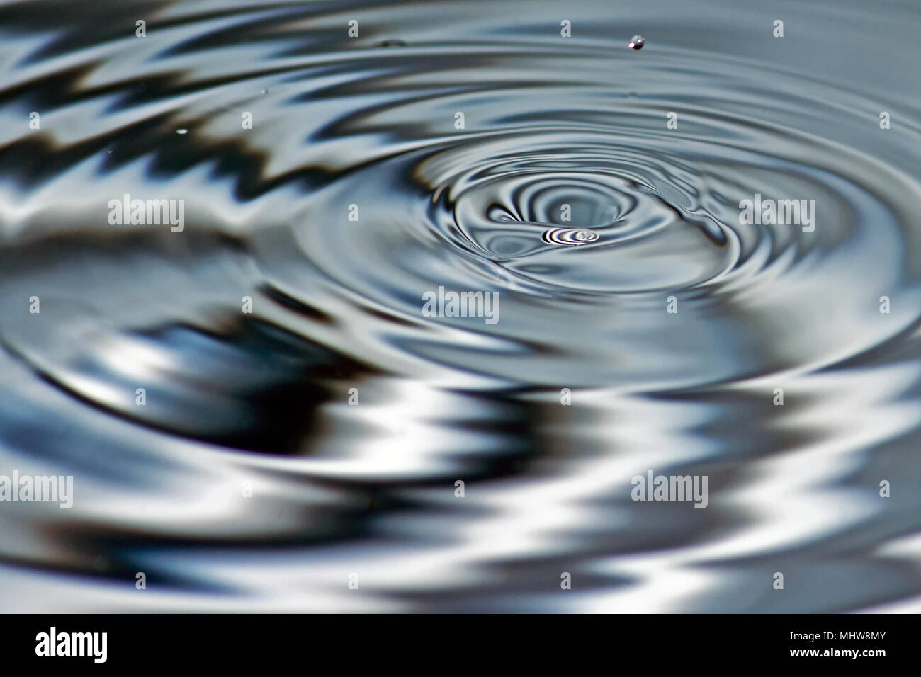 Wellen und Reflexionen durch den Eintrag von Wassertröpfchen in noch Wasser verursacht. Stockfoto