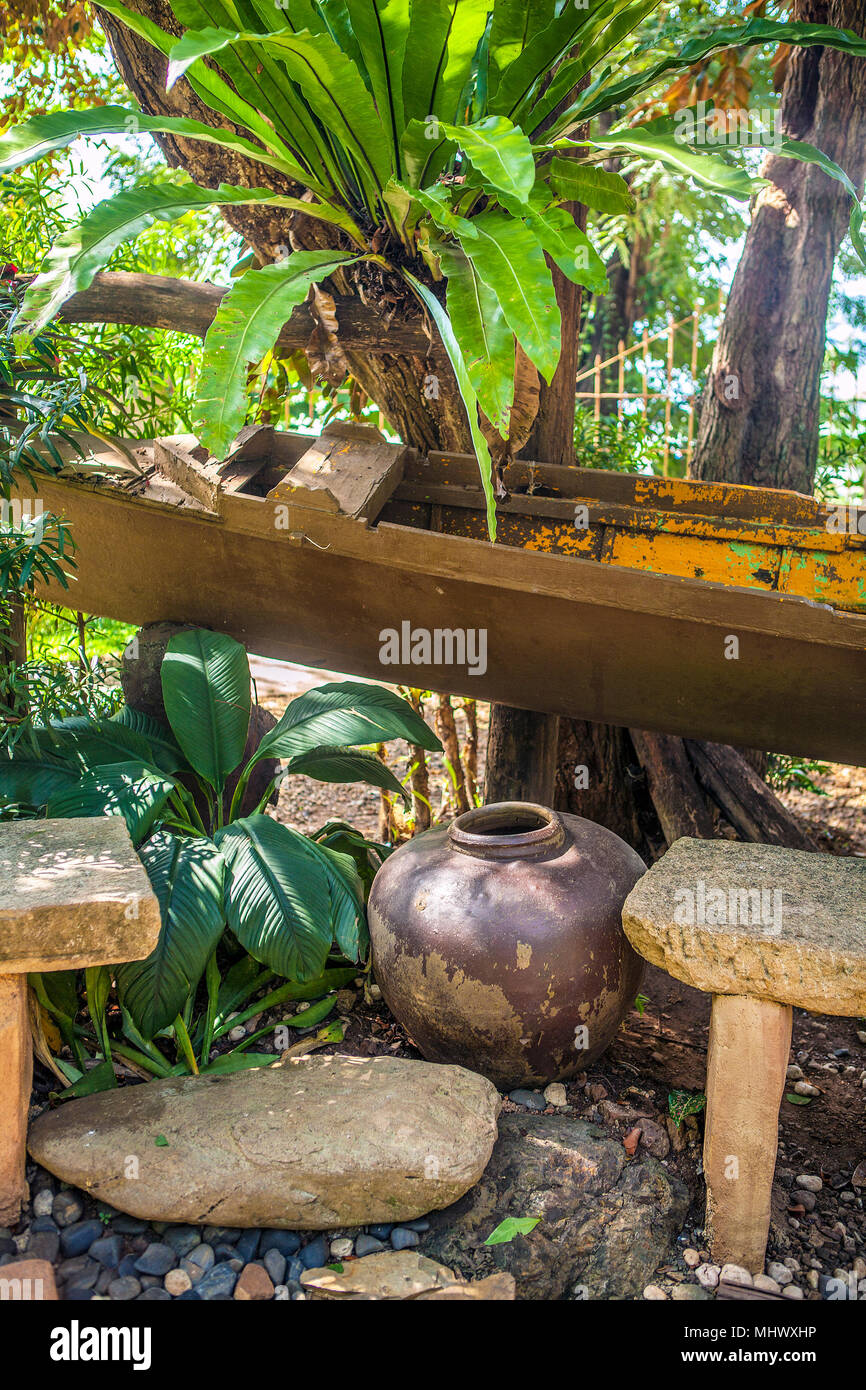 Ein Garten rest Sitzecke mit Anlagen konzipiert ist, eine alte Outrigger Kanu, Steinzeug Krug und Steinbänke in Puerto Princesa, Palawan, Philippinen Stockfoto
