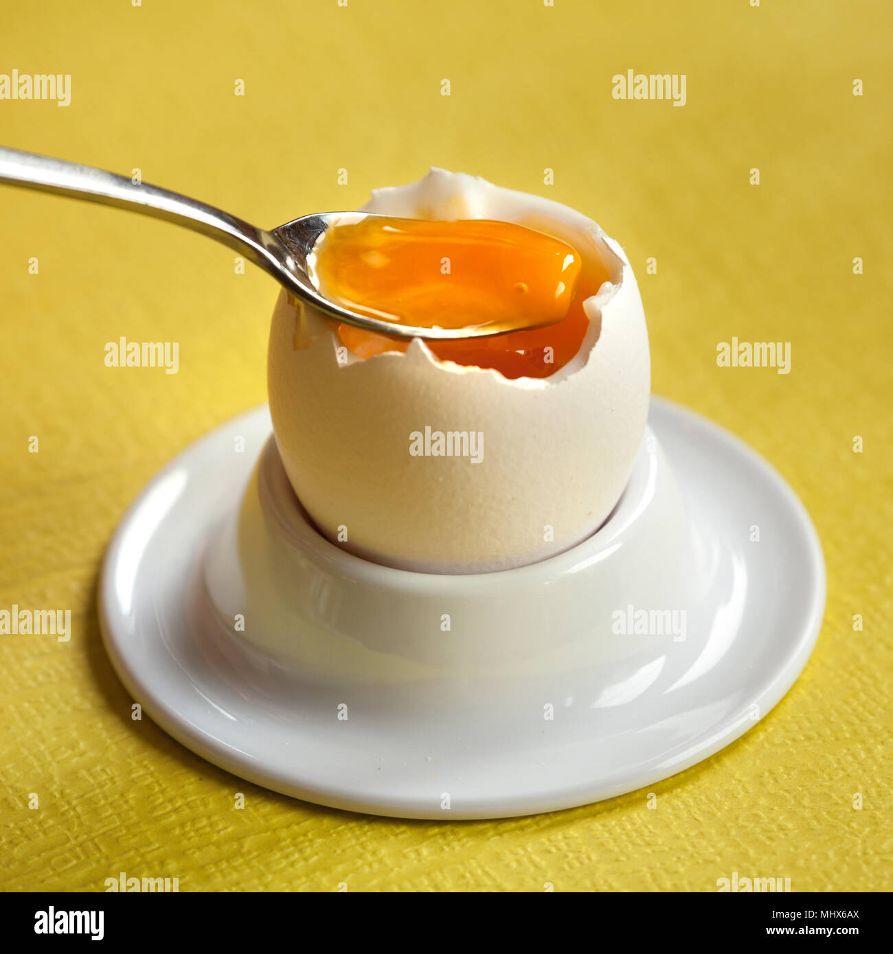 Weich gekochten Ei in einer Porzellan Eierbecher mit einem kleinen Löffel auf gelben Hintergrund. Stockfoto