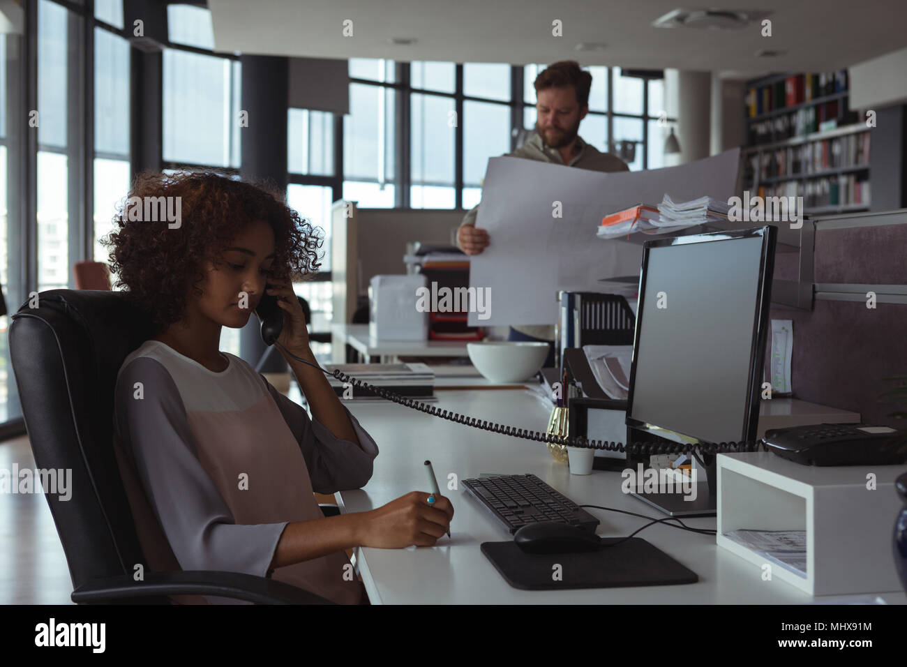 Weibliche Architekt am Telefon sprechen, während Kollege Kontrolle Blueprint Stockfoto