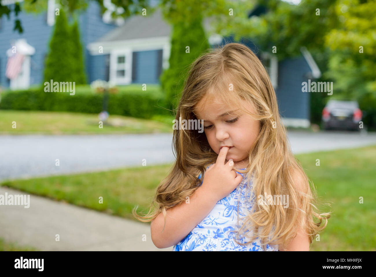 Mädchen mit dem Finger in den Mund, auf den Bürgersteig Stockfoto