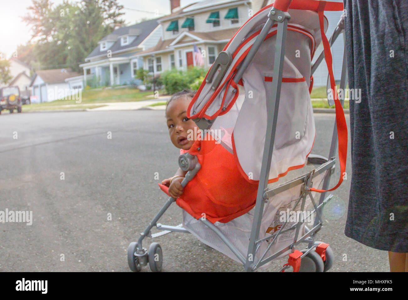 Baby Mädchen in Kinderwagen schaut über ihre Schulter auf suburban Bürgersteig, Porträt Stockfoto