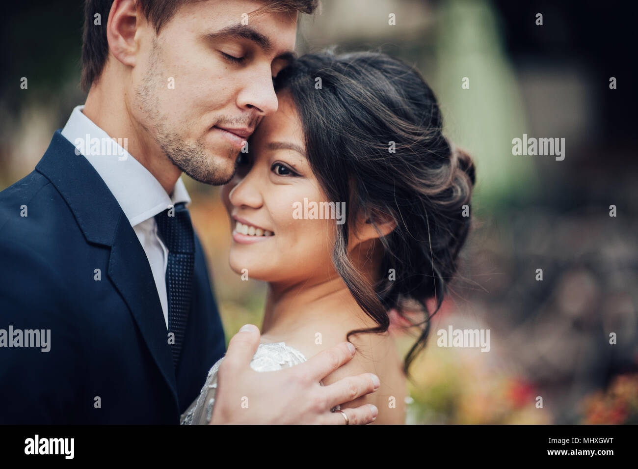 Bräutigam zärtlich umarmen asiatische Braut im weißen Kleid Stockfoto