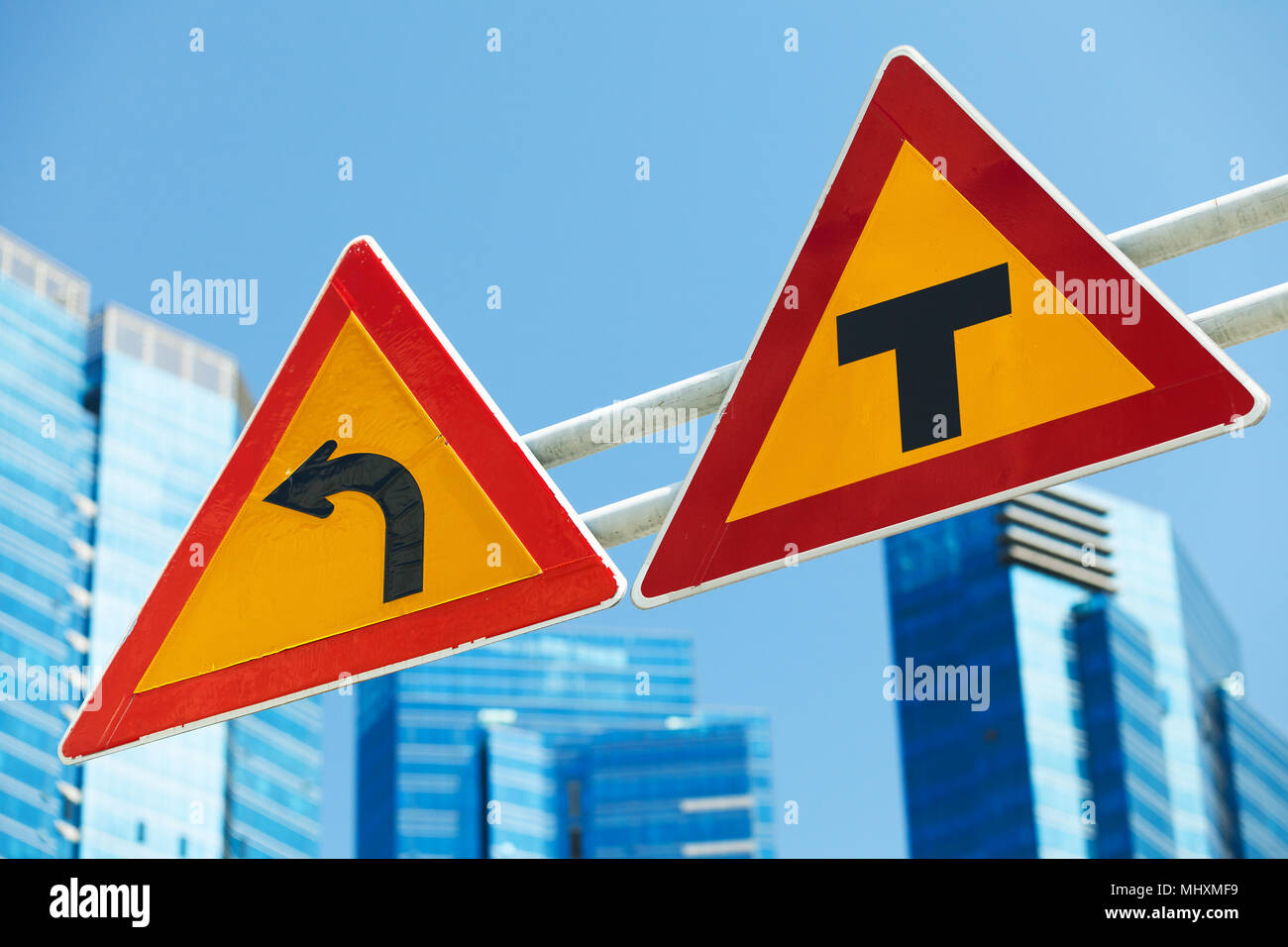 Gefährliche biegen Sie links ab und überqueren Straßen, Warnung Verkehrszeichen über Blue City Skyline Stockfoto