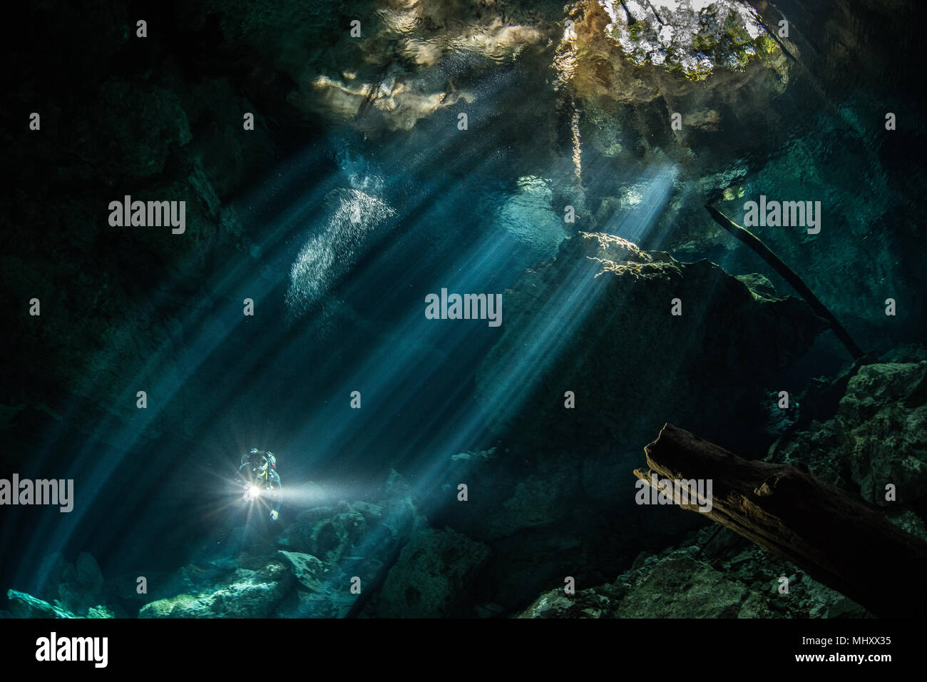 Männliche Taucher tauchen im unterirdischen Fluss (CENOTE) mit Sonnenstrahlen und Felsformationen, Tulum, Quintana Roo, Mexiko Stockfoto