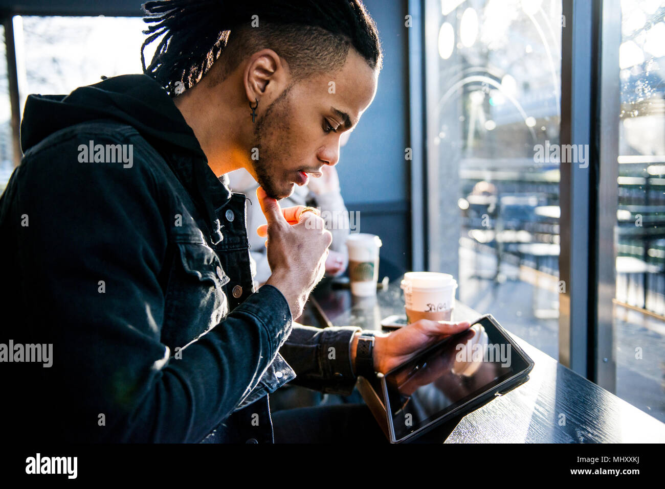 Junger Mann im Café sitzen, am digitalen Tablet, London, England, Großbritannien Stockfoto