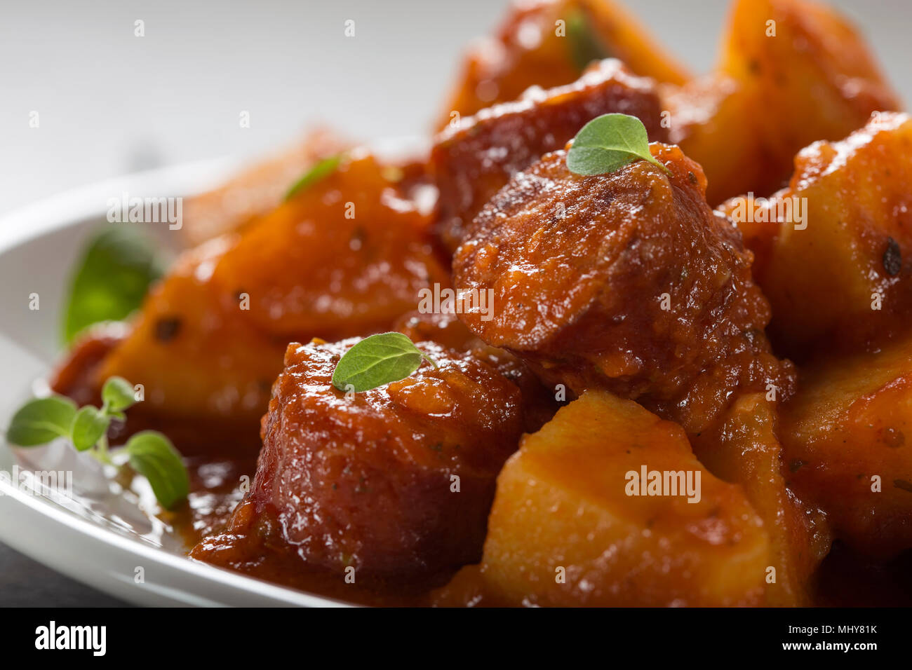 Kartoffeln Eintopf mit Schweinefleisch Wurstscheiben und Tomatensauce auf einem weißen Teller mit Oregano Blätter Stockfoto