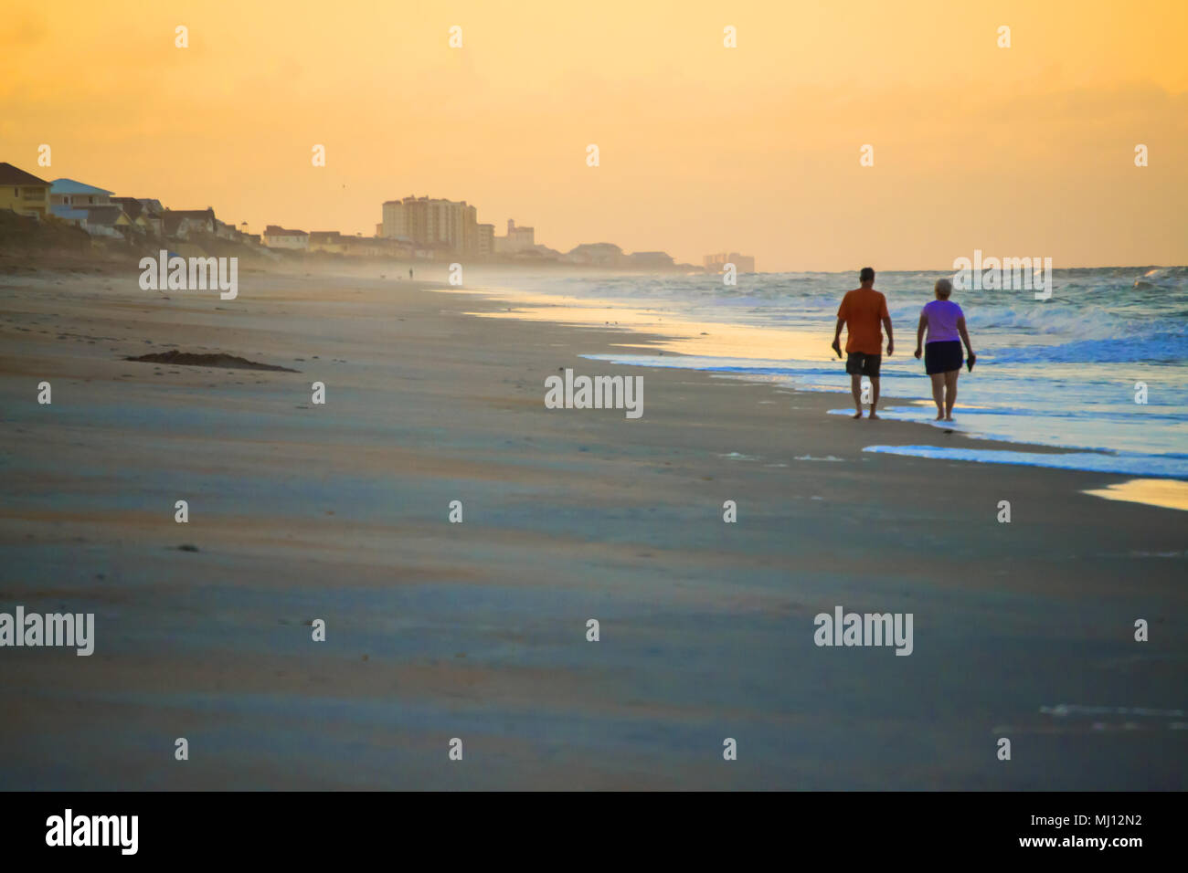 Ein älteres Paar, das bei Sonnenuntergang am Strand spazieren ging Stockfoto