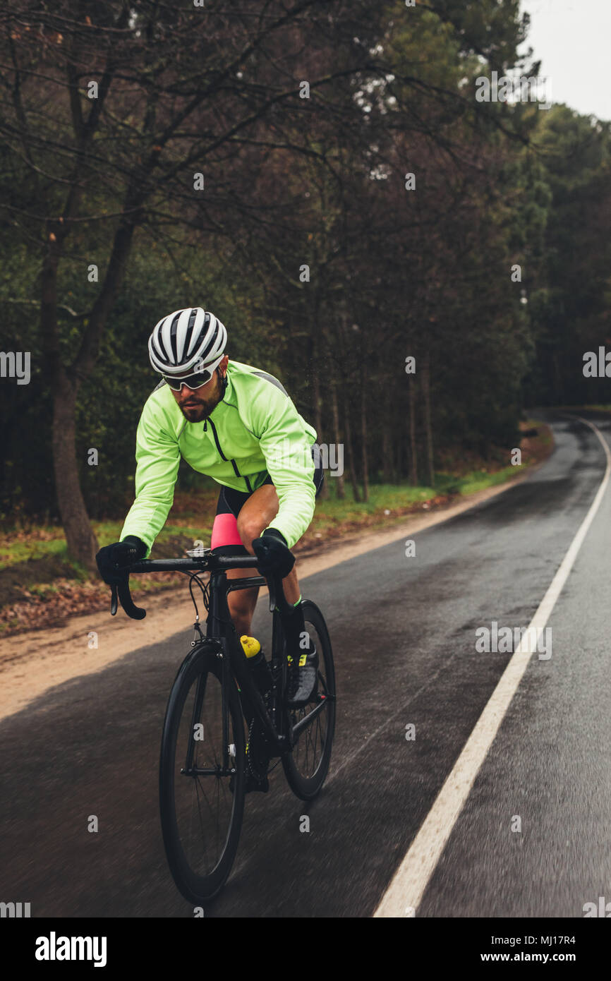 Sportler, der auf der Landstraße Fahrrad fährt. Profi-Radfahrer üben an einem regnerischen Tag. Stockfoto