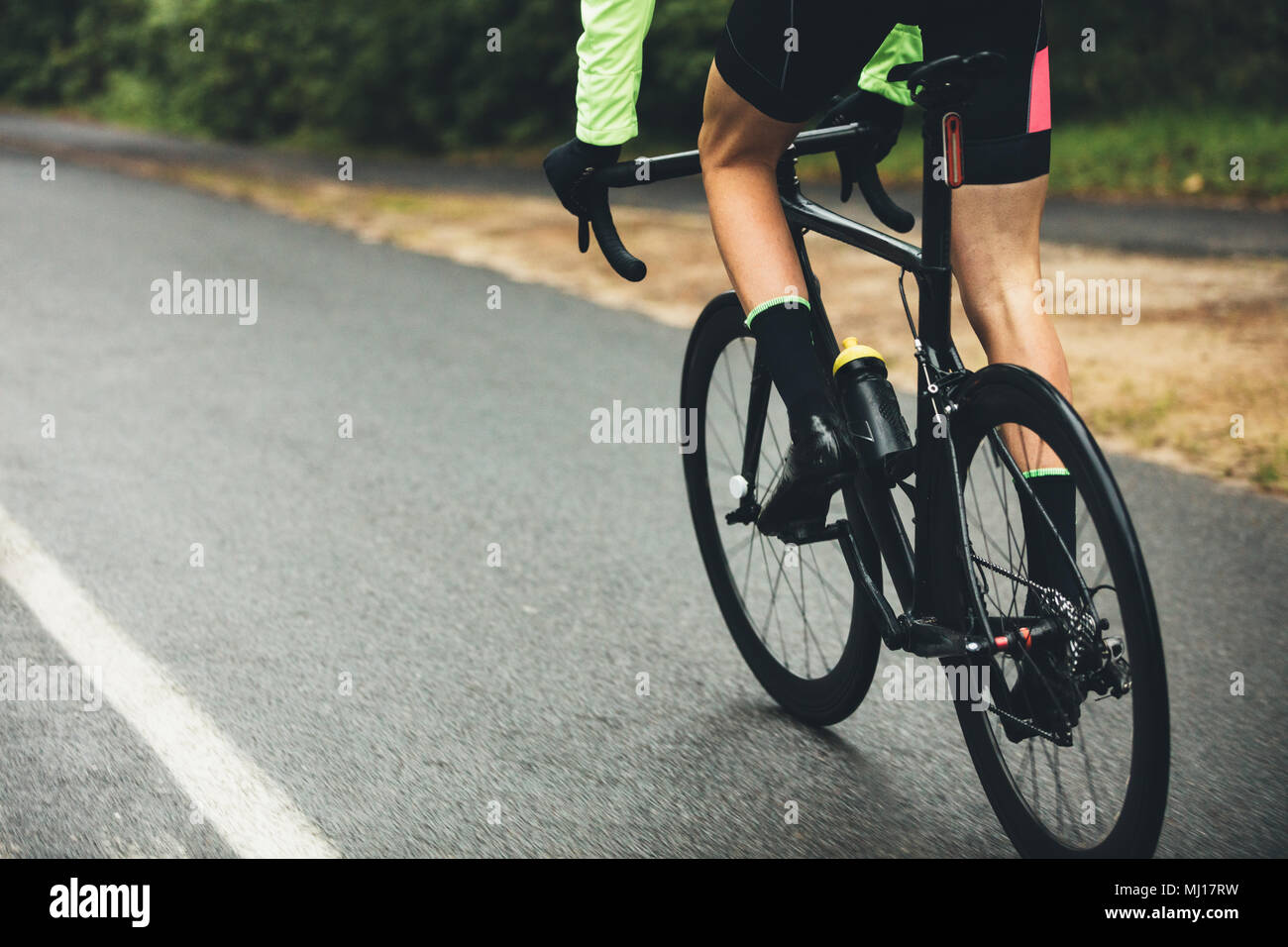 Männliche Athlet Radfahren auf der Landstraße. 7/8 Schuß des Menschen Reiten Fahrrad auf nasser Straße, Üben für einen Wettbewerb. Stockfoto