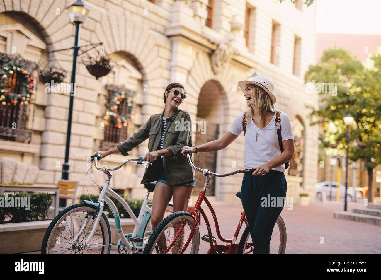 Glückliche junge Frau zu Fuß auf einer Straße mit ihren Bikes. Weibliche Freunde zu Fuß, mit dem Fahrrad über die Straße der Stadt. Stockfoto