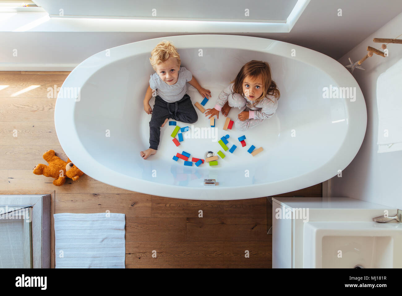 Kinder sitzen in der Badewanne mit Holz unterbauen und oben an der Kamera. Kleinen Jungen und Mädchen spielen in einer Badewanne zu Hause. Stockfoto
