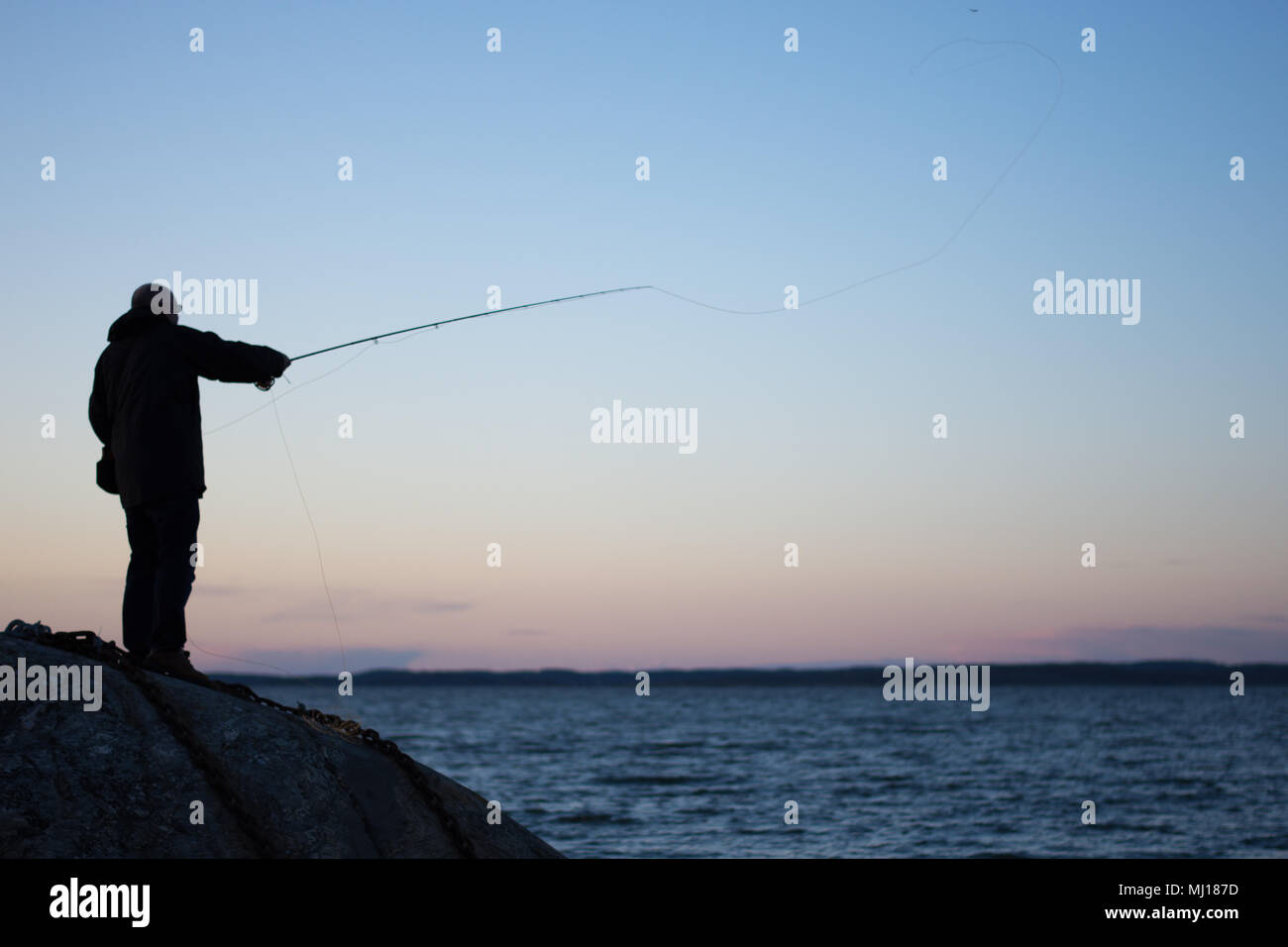 Silhouette der Angler Casting eine Fliege ins Meer in Richtung der untergehenden Sonne, die Fischerei auf Meerforelle in Schweden Stockfoto
