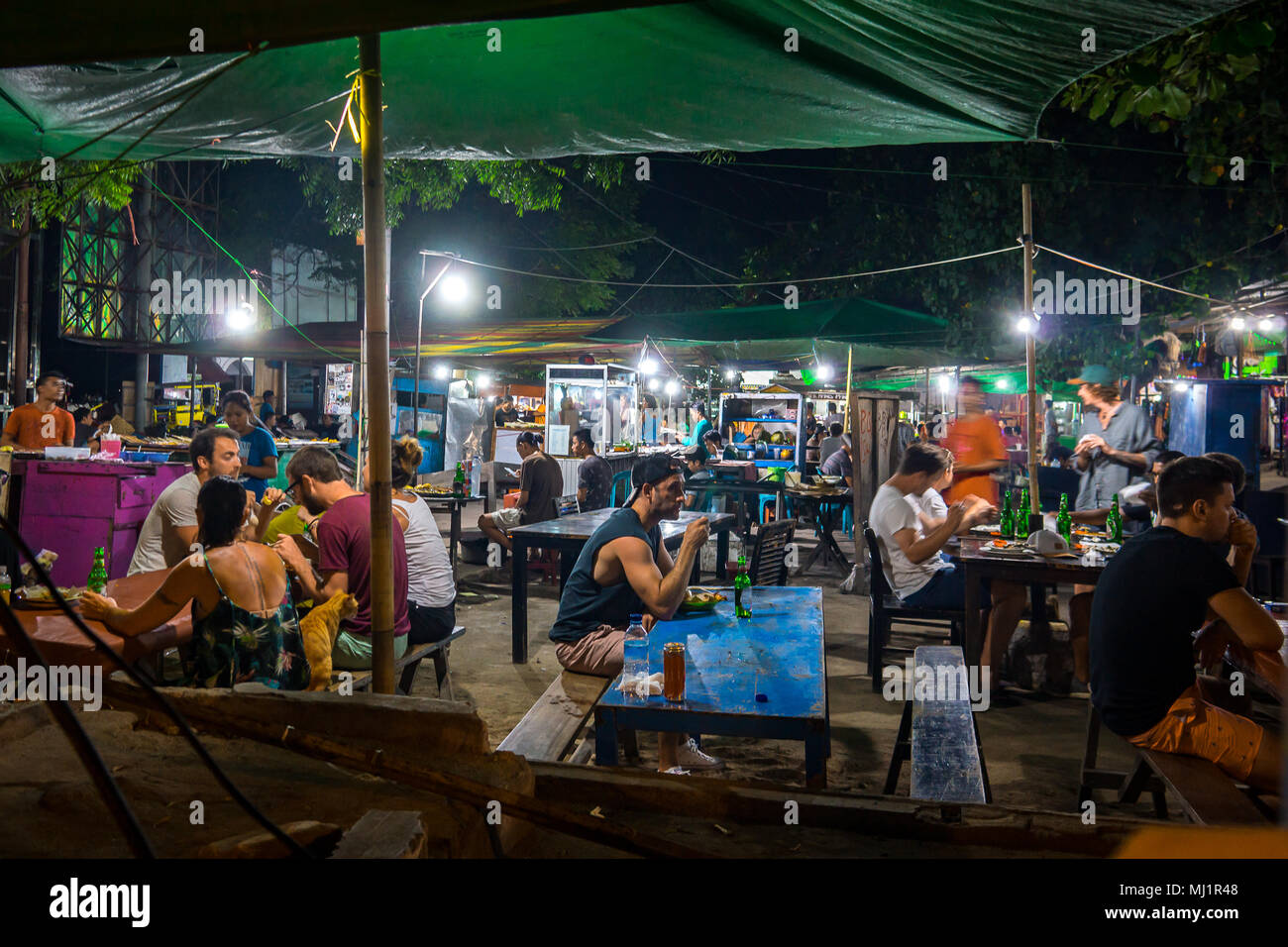 Europäische Touristen und Anwohnern saß im Licht der elektrischen Glühlampen an langen Tischen in verschiedenen streetfood in einem indonesischen Nightmarket, ein Stockfoto