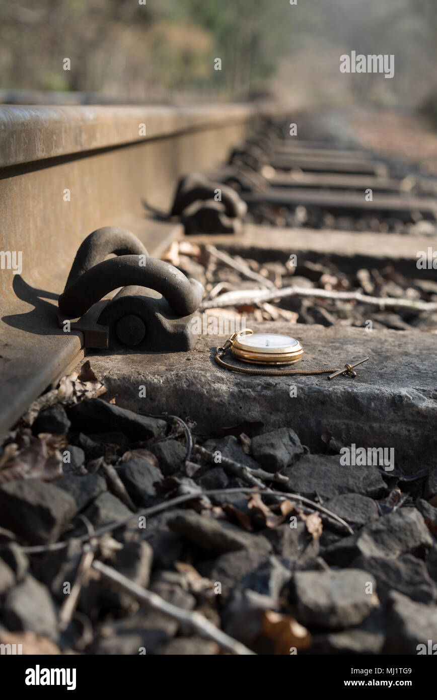 In der Nähe von antiken, Vintage gentleman Taschenuhr legen (nach oben) auf der Schwelle der Bahntrasse in die Ferne zu verschwinden. Verlorene Zeit Konzept. Stockfoto