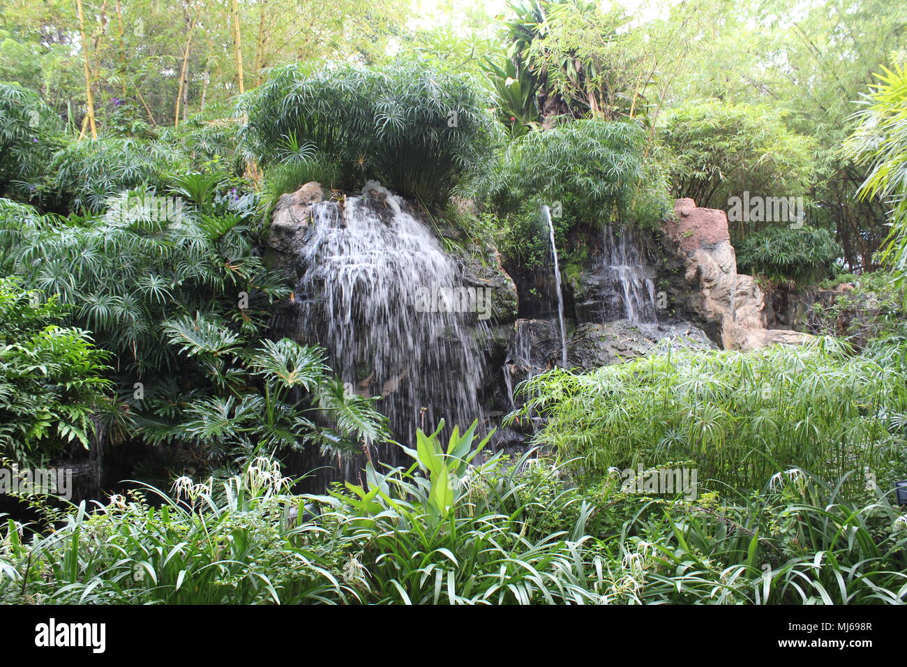 Künstlicher Wasserfall, umgeben von Bäumen und Pflanzen im Leela Palace, Bengaluru Stockfoto