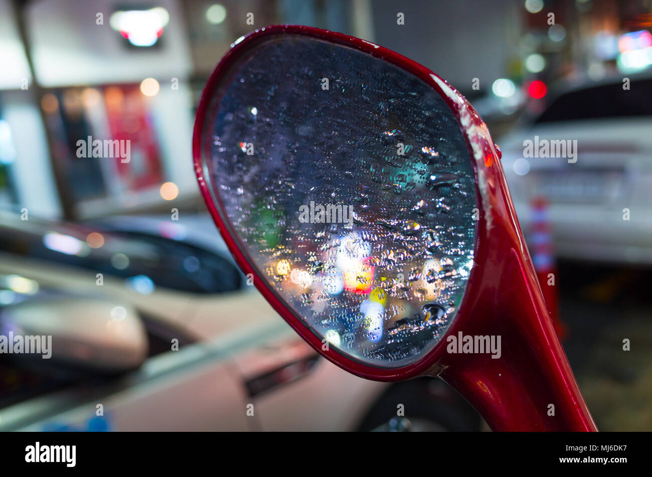 Bunte verschwommene Reflexionen und Regentropfen auf nassen scooter Spiegel Stockfoto