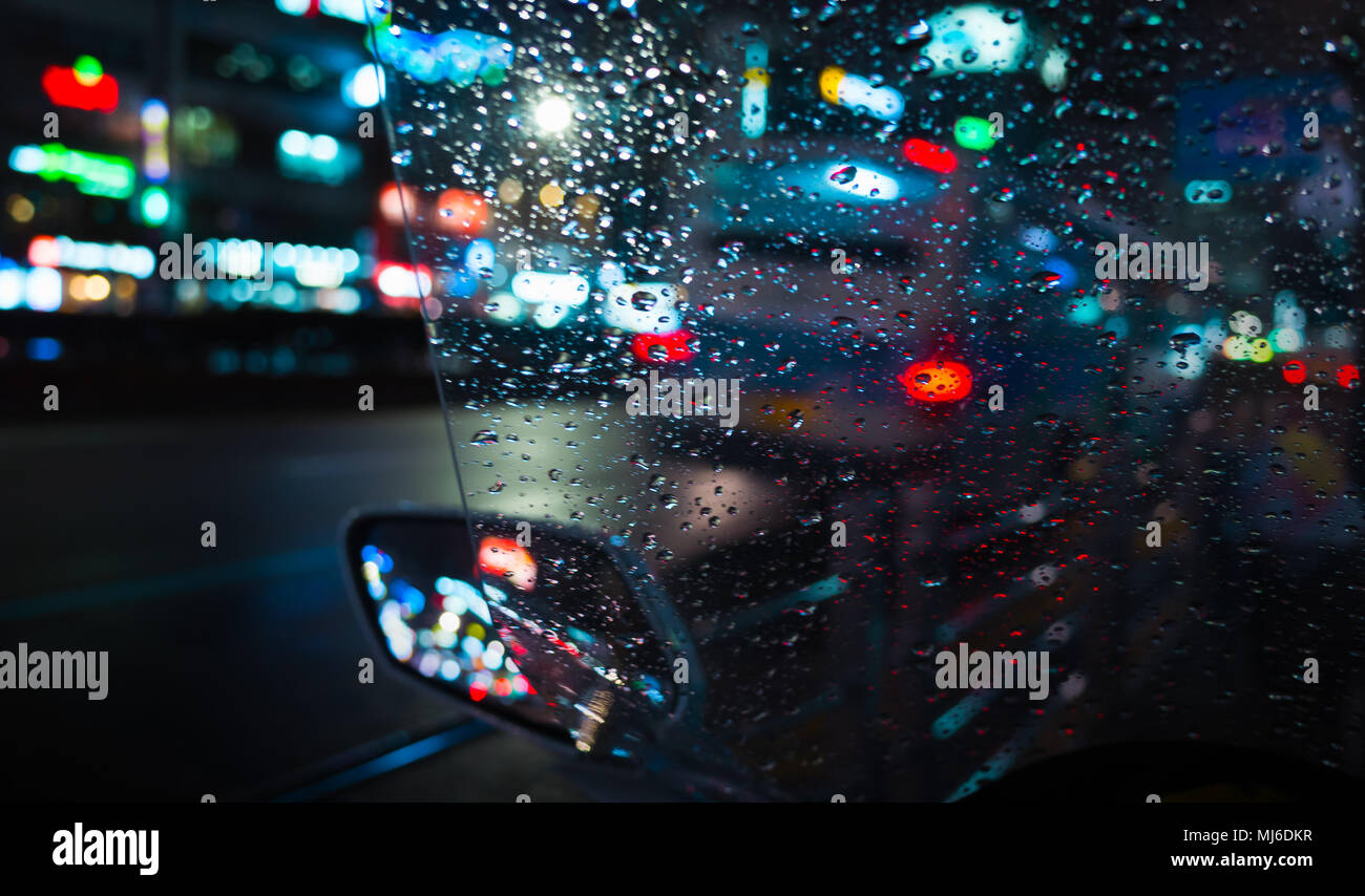 Abstract Night city unscharfen Hintergrund, bunte Reflexionen und Regentropfen auf nassen scooter Frontscheibe Stockfoto