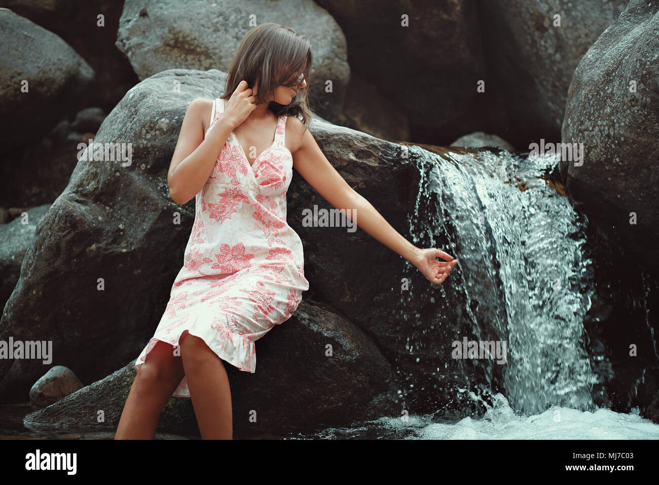 Junge Frau berühren einen Wasserfall. Sommer Kleid Stockfoto