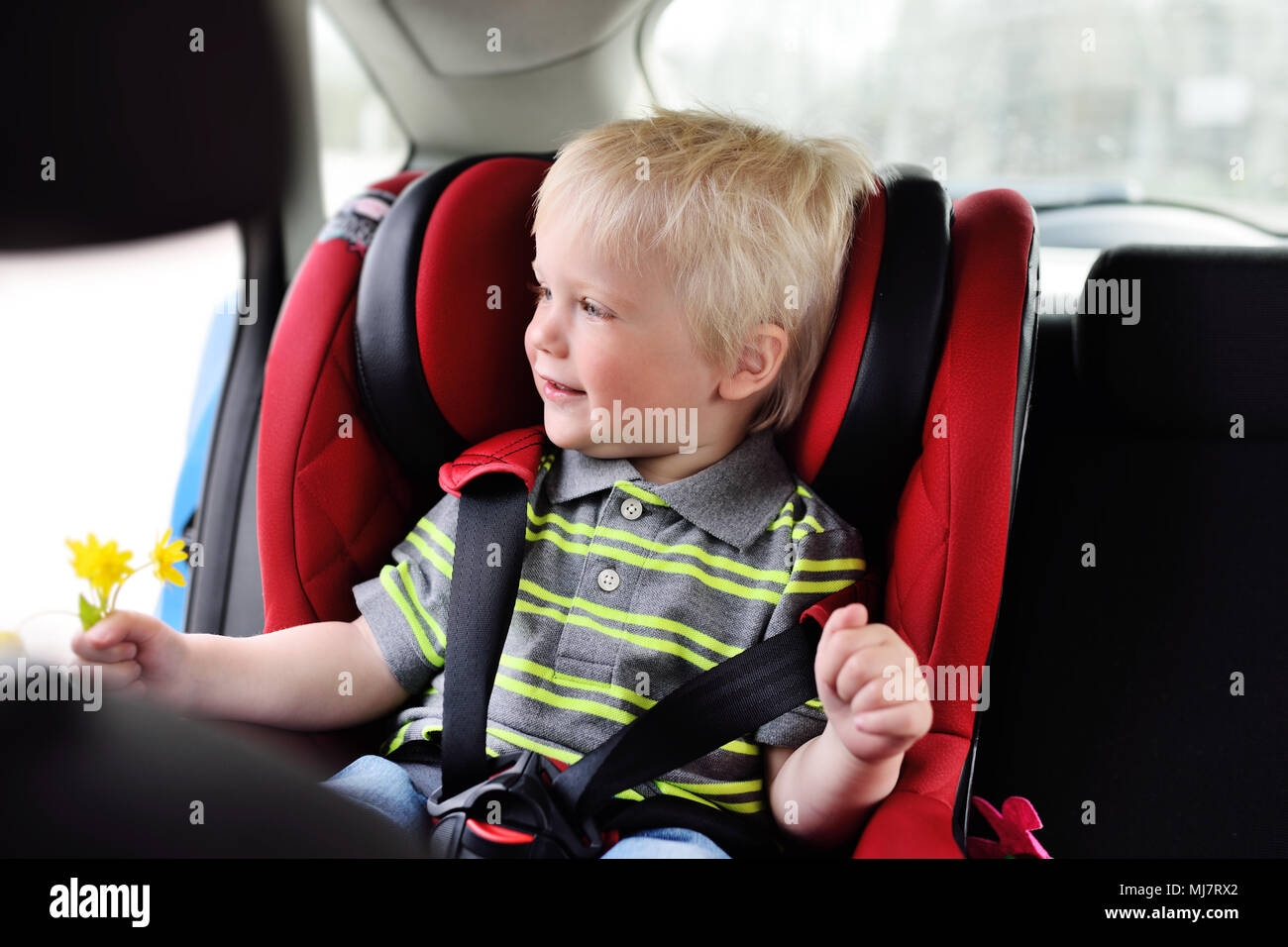 Porträt eines jungen Kindes von einem Jungen mit blonden Haaren in einem kinder Autositz. Stockfoto