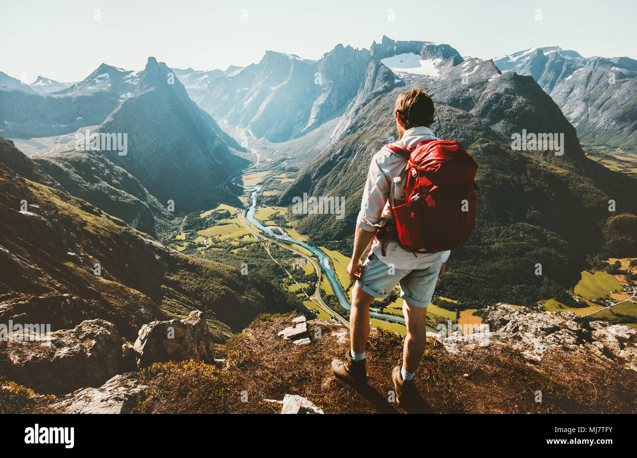 Wandern allein in Norwegen Bergen Mann mit roten Rucksack genießen Landschaft auf einer Klippe solo Gesund reisen lifestyle Konzept Aktiv Sommer Ferien Stockfoto
