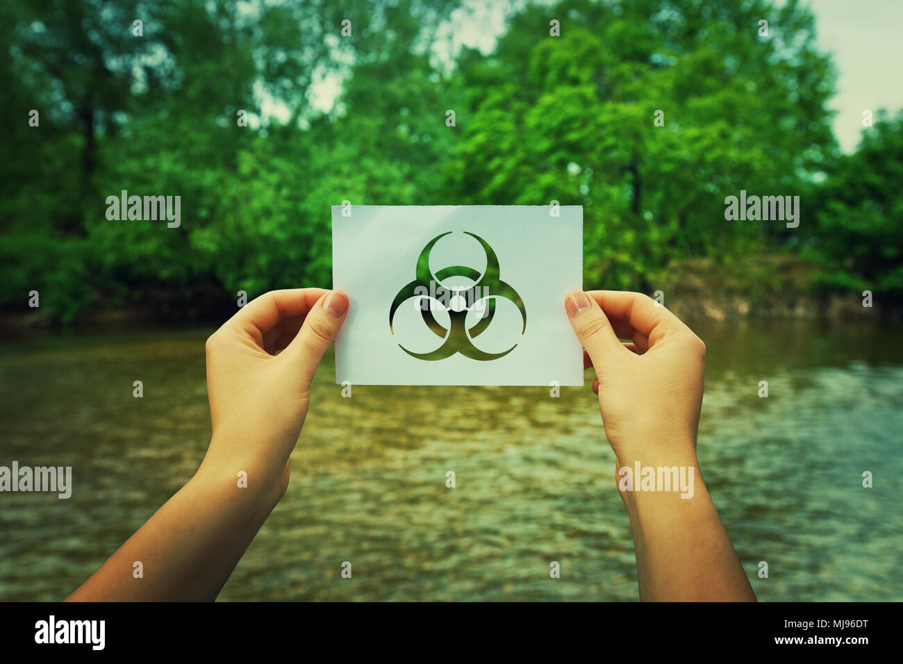 Frau Hände halten ein Blatt Papier mit einer Infektion Symbol in der Mitte der Natur in der Nähe von einem Fluss und den Wald. Biohazard Zeichen, Warnung Virus Stockfoto