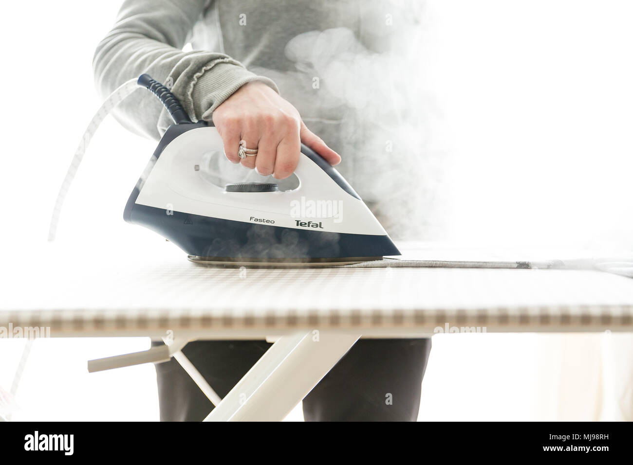 Bügeln mit dampfgenerator Bügeleisen. Nahaufnahme einer Hand, die heißen Dampf Bügeleisen auf dem Bügelbrett und Entfernen von Falten aus Stoff. Stockfoto