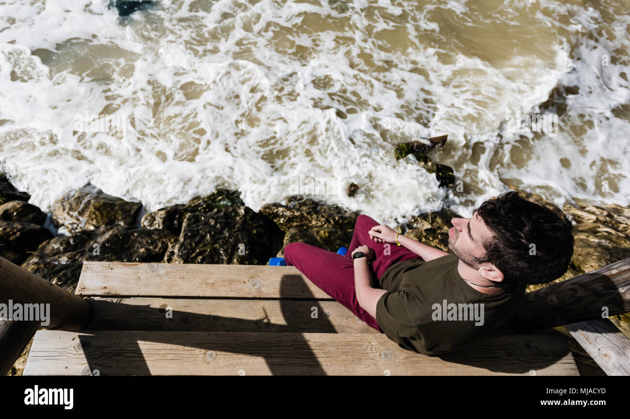 Junger Mann sitzt mit Blick auf das Meer in Overhead gesehen Stockfoto