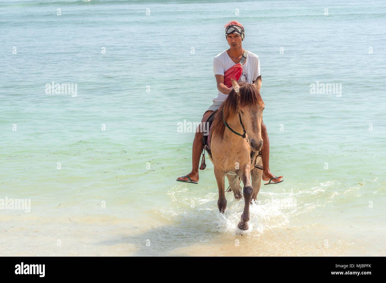 Indonesischer Mann ein Pferd reiten im blauen und grünen Wasser am Strand in Richtung Kamera, April 24, 2018, Gili Trawangan, Indonesien Stockfoto Indonesischer Mann ein Pferd reiten im blauen und grünen Wasser am Strand in Richtung Kamera, April 24, 2018, Gili Trawangan, Indonesien Stockfoto