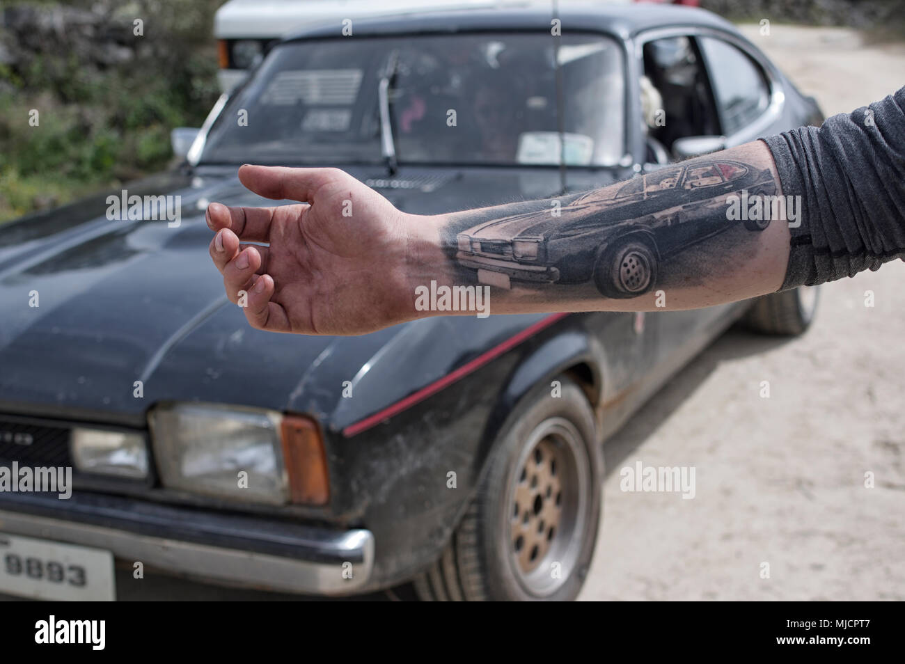 Mann mit Capri Tätowierung auf dem Arm und das Auto im Hintergrund Stockfoto