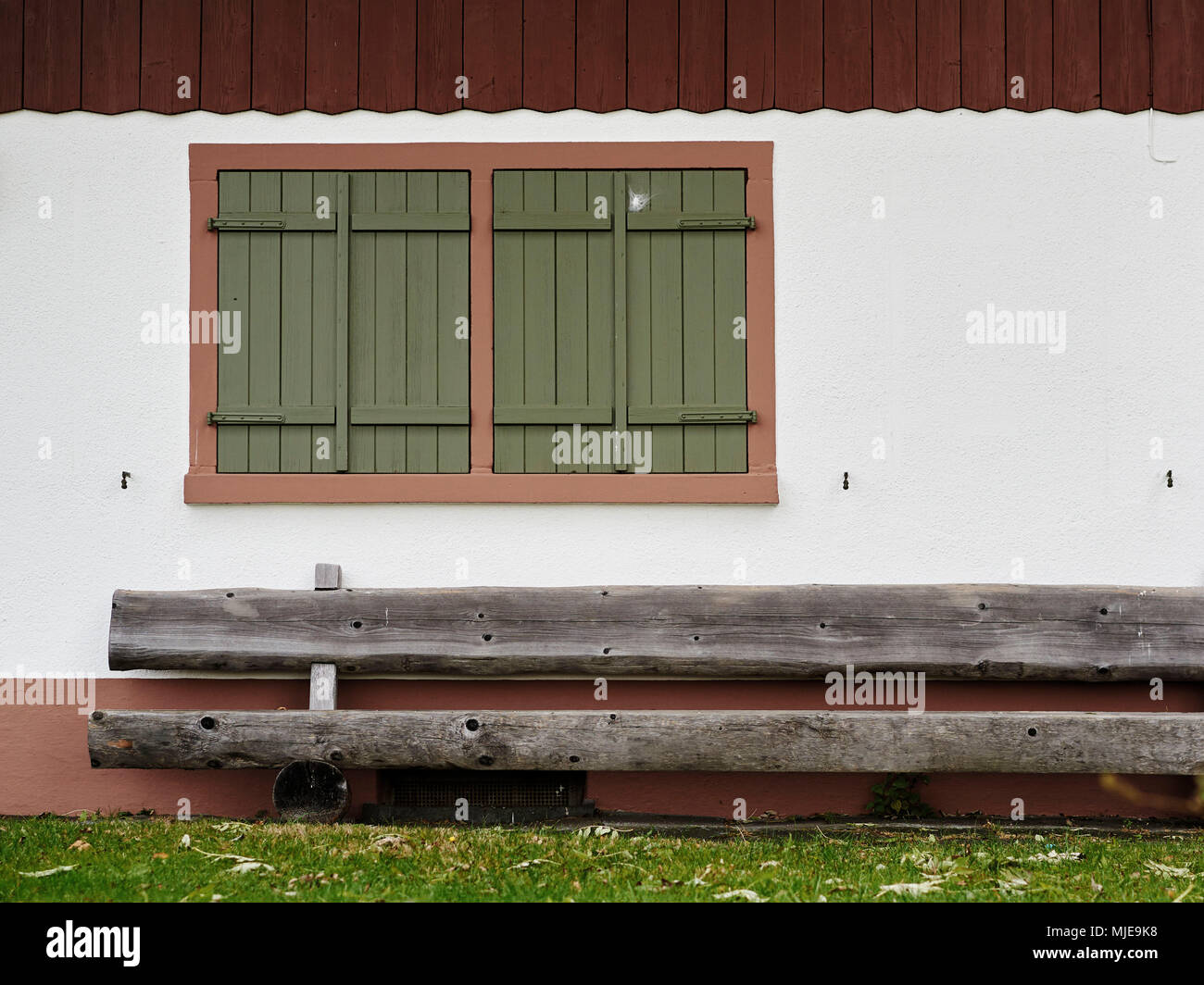 Blick auf eine Hauswand mit geschlossenem Fenster und eine Holzbank Stockfoto
