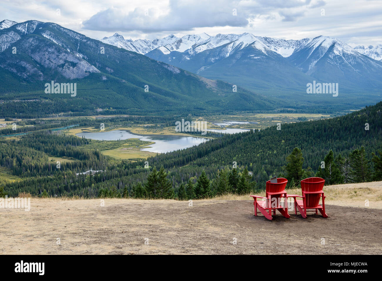 Zwei rote Stühle auf einem flachen Hang sind einladend zu sitzen und die schöne Aussicht auf das grüne Tal in der Nähe der Stadt Banff, Kanada Stockfoto