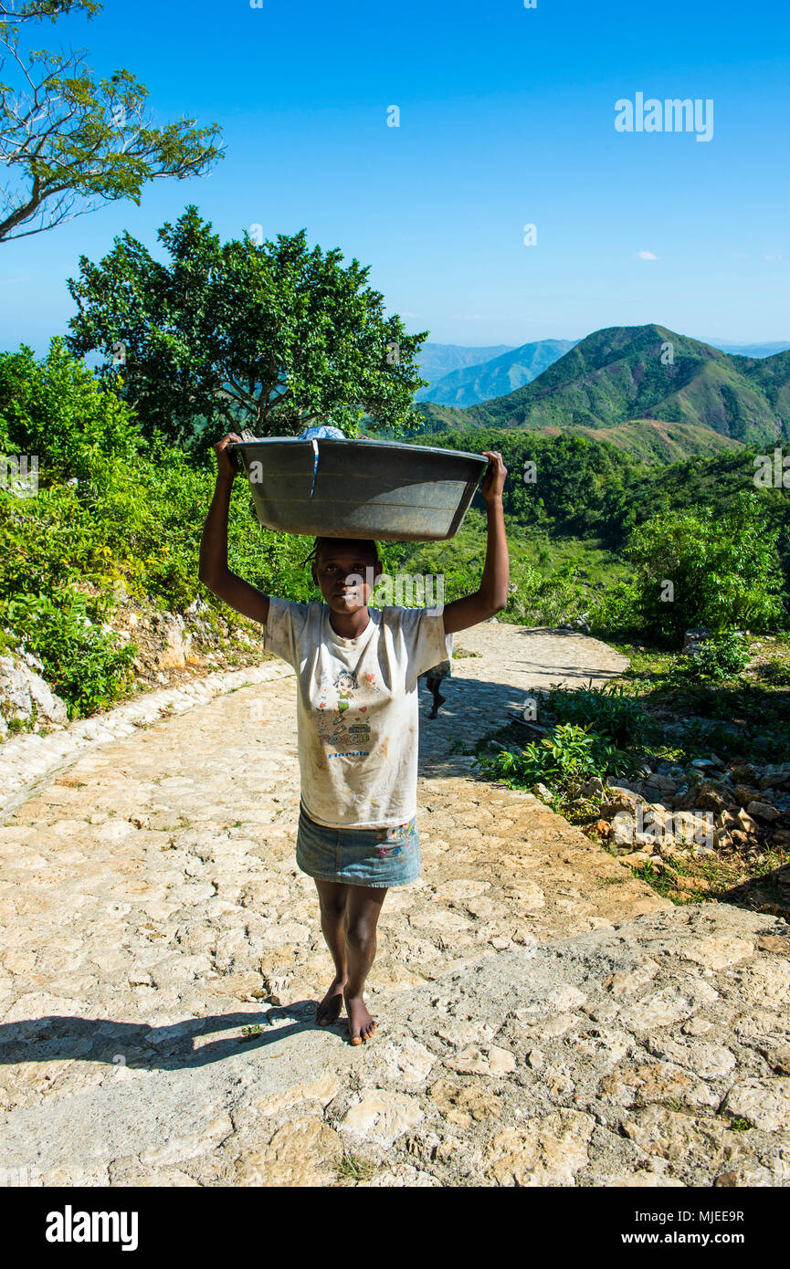 Frau, die einen riesigen Eimer mit Flaschen die steilen gepflasterten Straße, die zum Weltkulturerbe der Unesco die Citadelle Laferriere, Cap Haitien, Haiti, Karibik Stockfoto