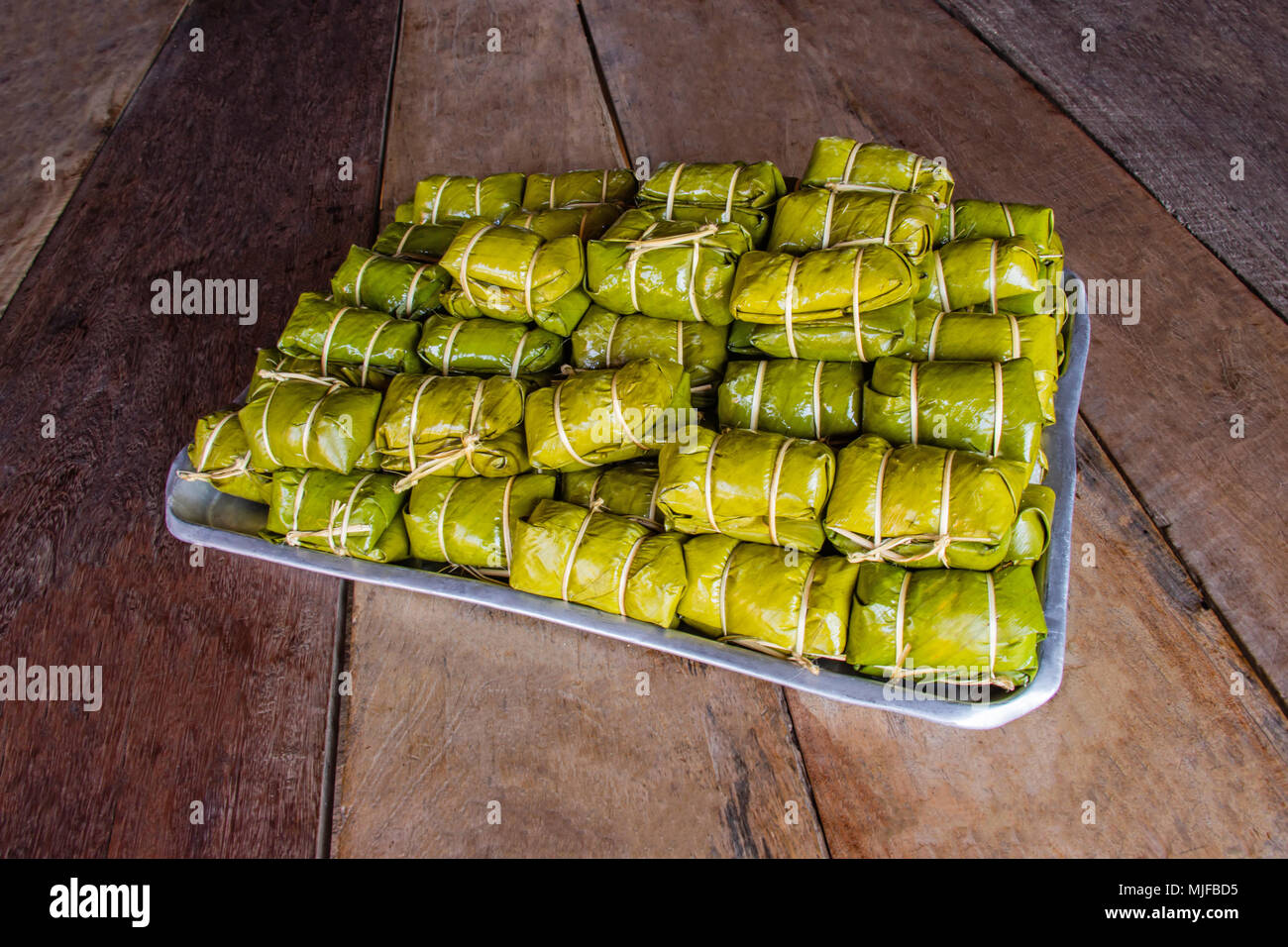 Bananen mit klebrigen Reis mit Blatt auf braunem Holz- Hintergrund gewickelt. Khao Tom Mat. Stockfoto