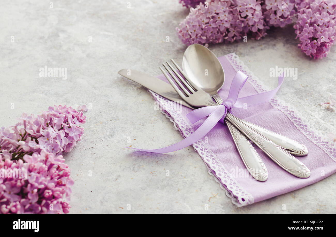 Frühling Tischdekoration mit lila Blüten. Elegante Tischdekoration mit lila Blüten, violett serviette und vintage Besteck auf rustikalen Hintergrund. Stockfoto