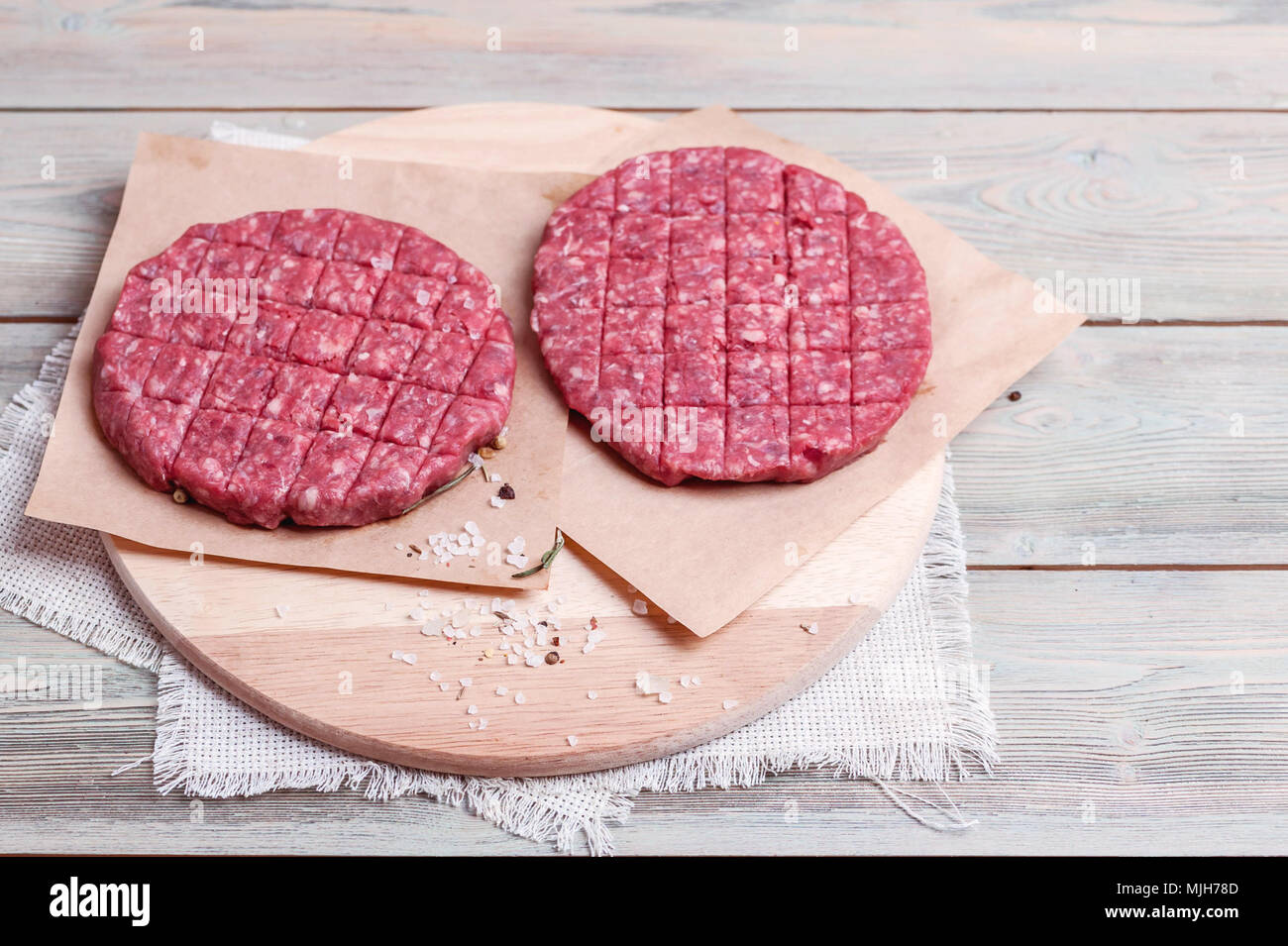 Rohes Rindfleisch Hamburger mit Gewürze auf einem runden hölzernen Schneidebrett Stockfoto