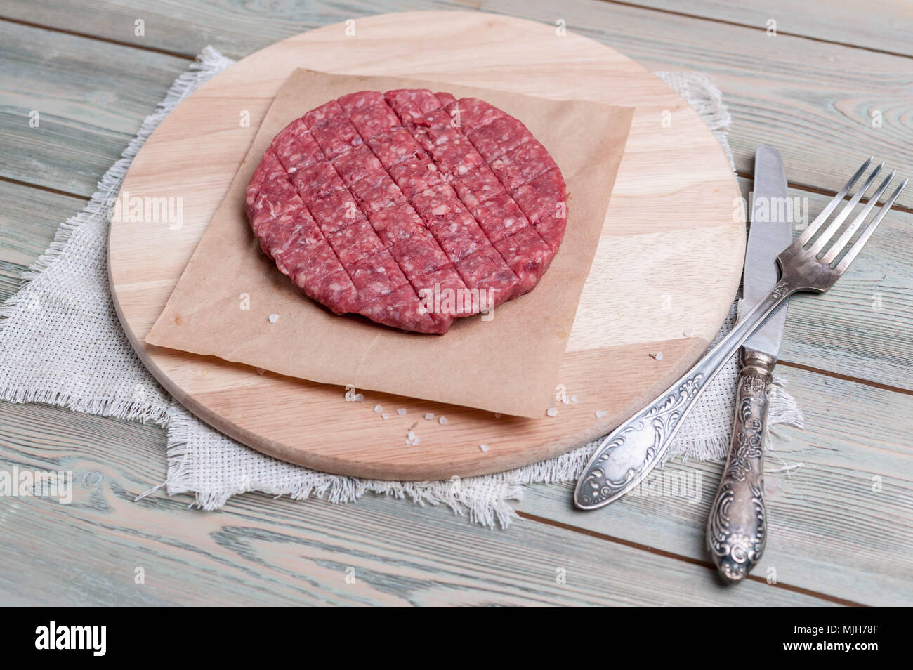 Rohes Rindfleisch Hamburger mit Gewürze auf einem runden hölzernen Schneidebrett Stockfoto